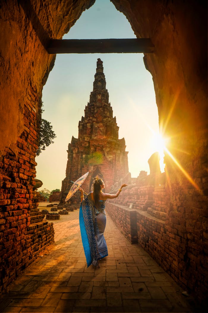 services-06 A woman in traditional wear stands with an umbrella at a historic Ayutthaya temple during sunset.