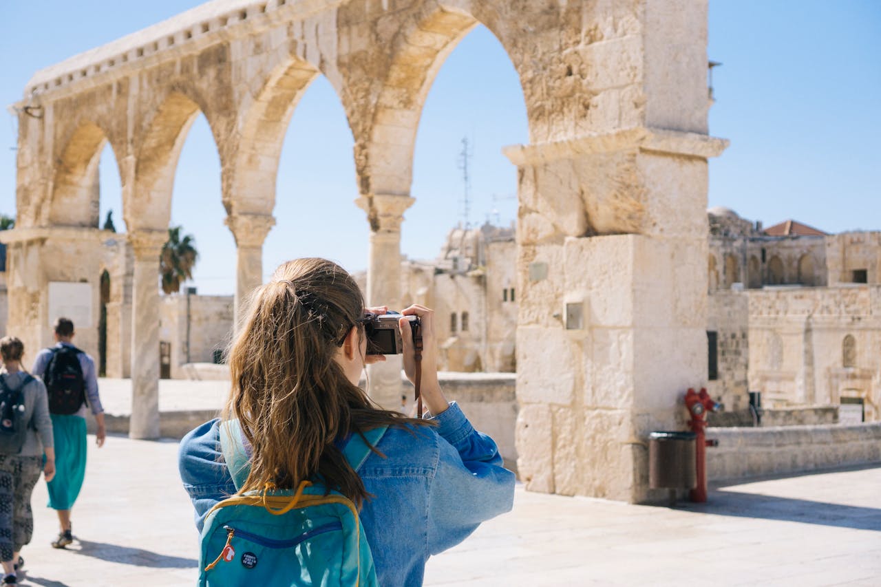 about-bg A tourist photographs the ancient stone arches in Jerusalem's Old Town, capturing the essence of travel and history.