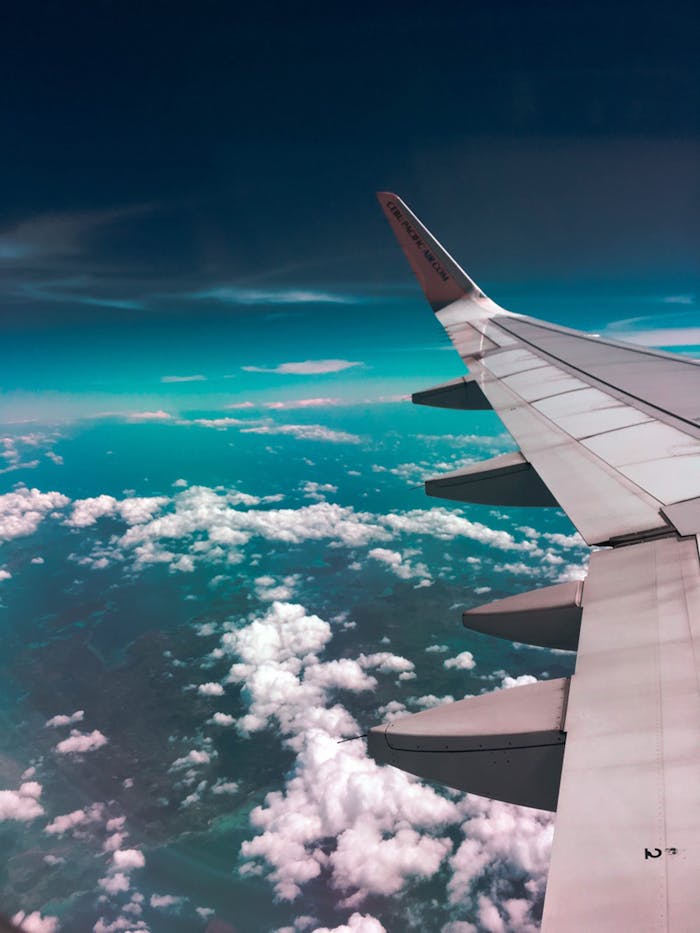 get-in-touch Aerial view of airplane wing over fluffy clouds with a deep turquoise sky.